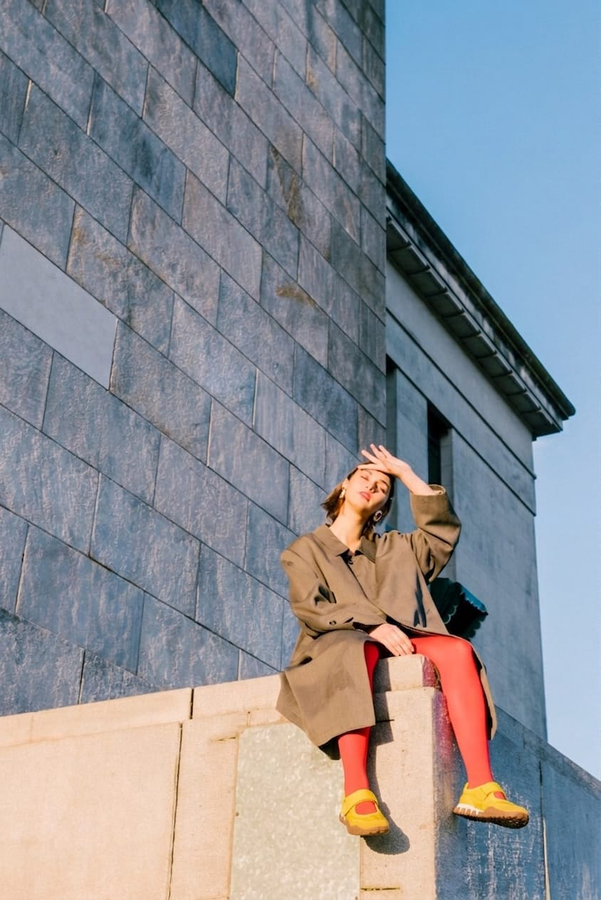 Woman in an oversized coat wearing bright shoes against modern architecture